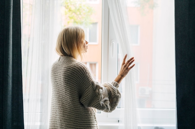 Kostenloses Foto seitenansicht der melancholischen frau zu hause während der pandemie, die durch das fenster schaut