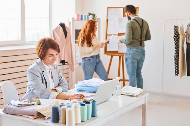 Seitenansicht der Modedesignerin, die im Atelier mit Kollegen und Laptop arbeitet