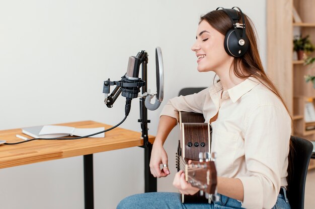 Seitenansicht der Musikerin, die Lied aufnimmt, während zu Hause akustische Gitarre spielt