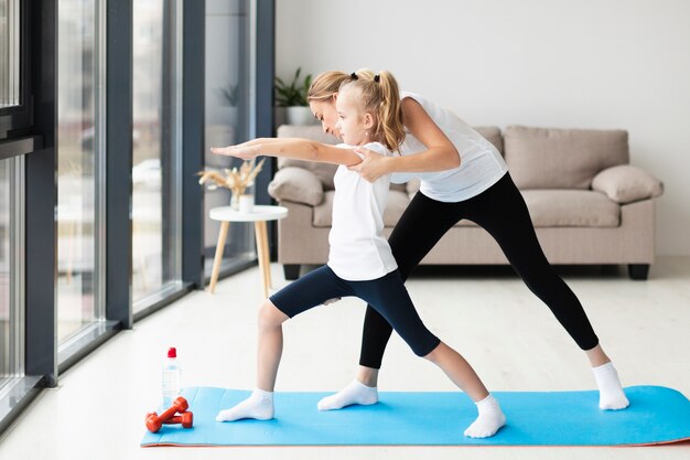 Seitenansicht der Mutter, die Tochter hilft, Yoga zu tun