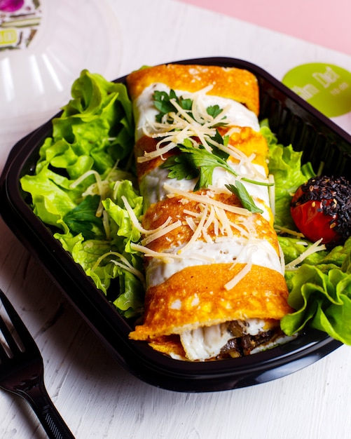 Kostenloses Foto seitenansicht der pfannkuchenrolle mit hühnergemüse und käse auf salat im lieferkasten