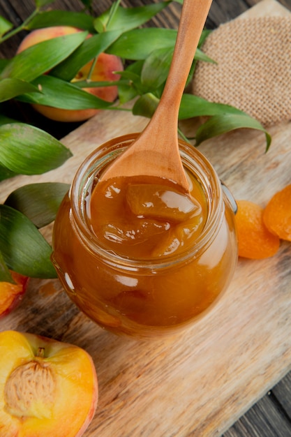 Seitenansicht der Pfirsichmarmelade in einem Glas mit Holzlöffel auf hölzernem Hintergrund