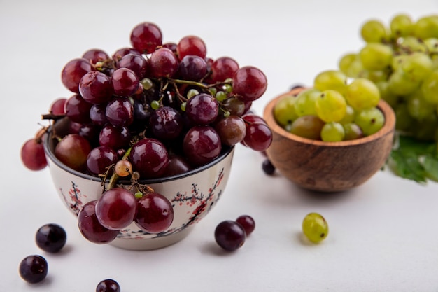 Seitenansicht der roten Traube und der weißen Traubenbeeren in den Schalen mit der weißen Traube der Weinbeeren und den Blättern auf weißem Hintergrund