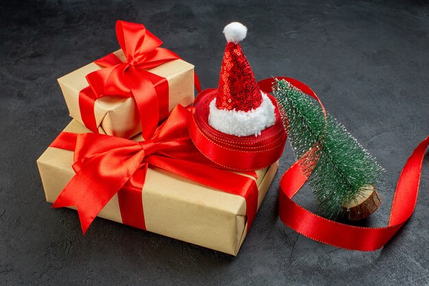 Seitenansicht der schönen Geschenke mit rotem Band und Weihnachtsmannhut-Weihnachtsbaum auf dunklem Tisch