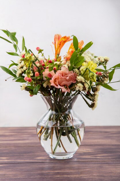 Seitenansicht der schönen verschiedenen bunten Blumen mit Blättern auf einer Glasvase auf einem Holztisch auf weißer Oberfläche