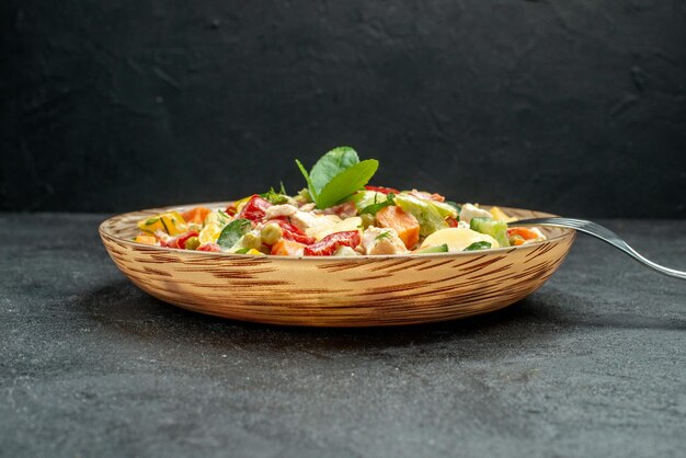 Seitenansicht der Schüssel Gemüsesalat mit Gabel auf der Seite auf dunkelgrauem Tisch auf dunkelgrauem Hintergrund