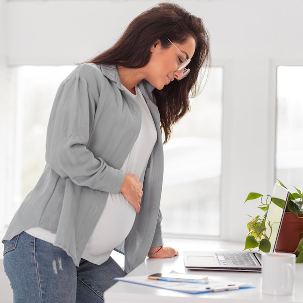 Seitenansicht der schwangeren Frau, die zu Hause am Laptop arbeitet