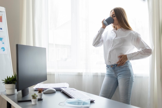 Seitenansicht der schwangeren Geschäftsfrau, die Kaffee im Büro trinkt