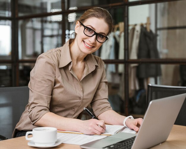 Seitenansicht der Smiley-Geschäftsfrau, die mit Laptop am Schreibtisch arbeitet