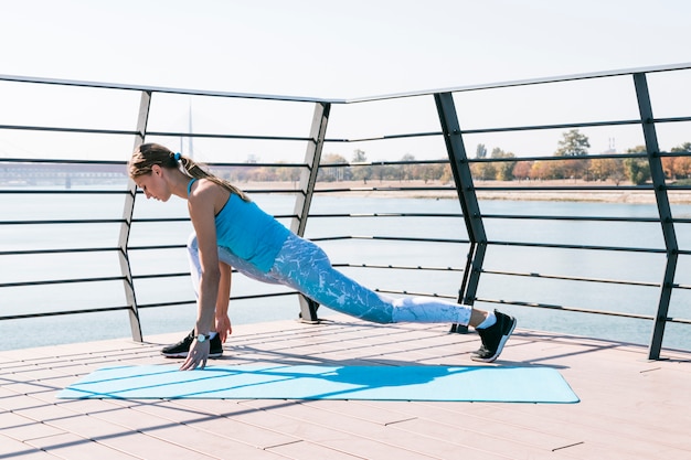 Seitenansicht der sportiven jungen Frau, die auf Brücke nahe dem See trainiert