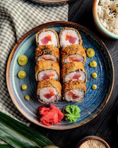 Seitenansicht der Sushi-Rolle mit Krabben und Thunfisch auf einem Teller mit Ingwer und Wasabi auf Holz