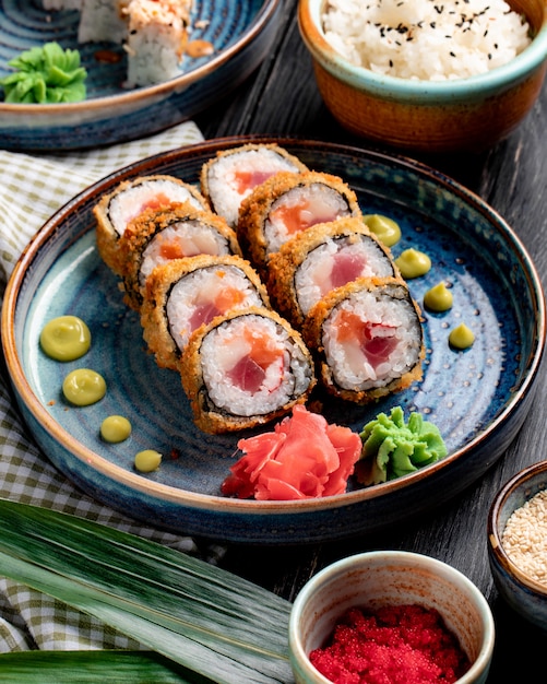 Seitenansicht der Sushi-Rolle mit Krabben und Thunfisch auf einem Teller mit Ingwer und Wasabi auf Holzoberfläche