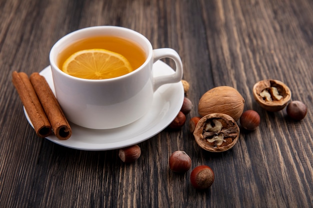 Seitenansicht der Tasse des heißen Wirbels mit Zimt auf Untertasse und Nusswalnüssen auf hölzernem Hintergrund