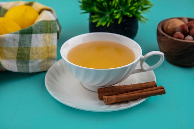 Seitenansicht der tasse des heißen wirbels mit zimt auf untertasse und zitronen mit nüssen auf blauem hintergrund