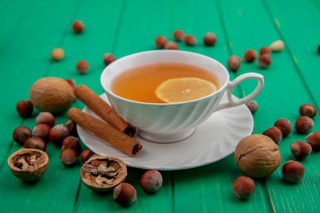 Seitenansicht der tasse des heißen wirbels mit zitrone innen und zimt auf untertasse mit nüssen und walnüssen herum auf grünem hintergrund