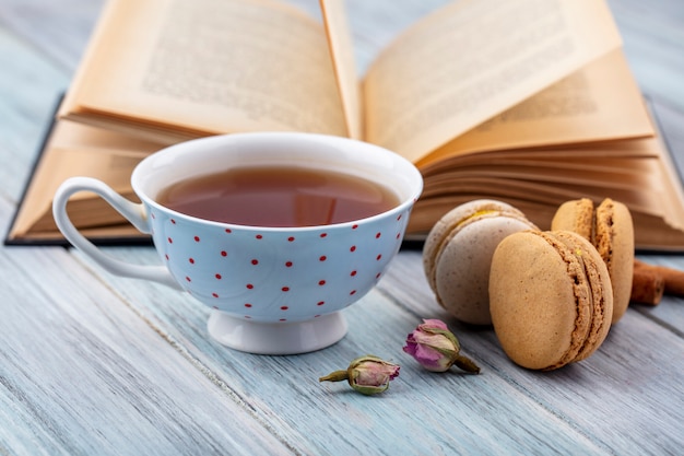 Seitenansicht der Tasse Tee mit Macarons und einem offenen Buch auf einer grauen Oberfläche