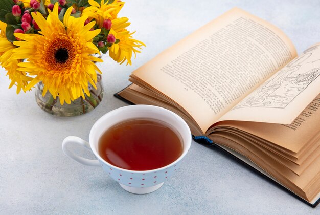 Seitenansicht der Tasse Tee und der Blumen mit offenem Buch auf weißer Oberfläche