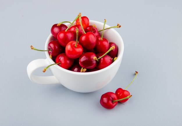 Seitenansicht der Tasse voller roter Kirschen auf der linken Seite und des weißen Tisches