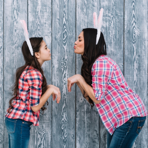 Seitenansicht der Tochter und der Mutter, die wie ein Häschen aufwerfen gegen grauen hölzernen Hintergrund aufwirft