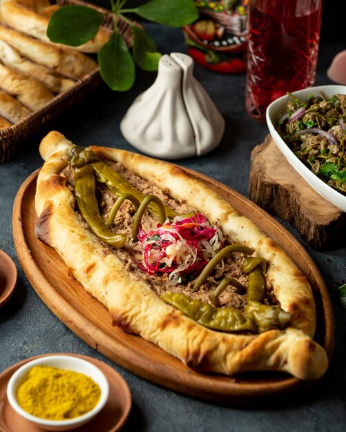 Seitenansicht der traditionellen georgischen Küche Khachapuri mit Fleisch und eingelegtem heißem Chili-grünem Pfeffer in der Holzplatte