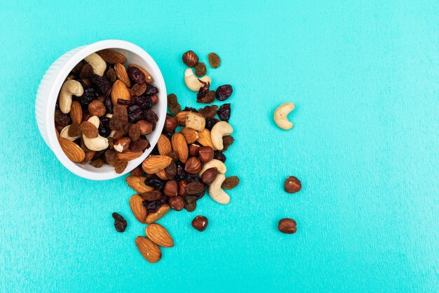 Seitenansicht der verschiedenen Arten von Snacks als Nüsse mit getrockneten Früchten in der Schüssel auf blauem Hintergrund horizontal