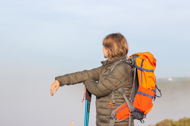 Seitenansicht der Wanderin an einem sonnigen Tag. Frau mit großem orangefarbenem Rucksack, der auf der Wiese steht. Hobby, aktives Lifestyle-Konzept