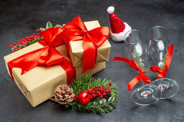 Seitenansicht der Weihnachtsstimmung mit schönen Geschenken mit bogenförmigem Band und Tannenzweigdekorationszubehör Weihnachtsmann hat gefallene Glasbecher Nadelbaumkegel auf einem dunklen Hintergrund