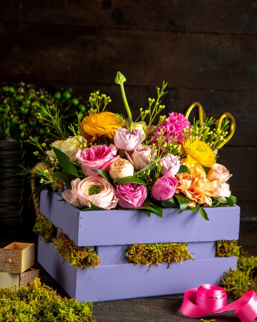 Seitenansicht der Zusammensetzung von rosa und lila Rosen und Ranunkelblumen in der Holzkiste