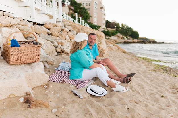 Seitenansicht des älteren Touristenpaares, das Picknick am Strand hat