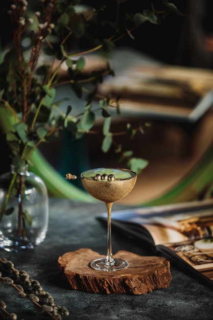 Seitenansicht des Alkoholcocktails mit Kiwi in einem goldenen Glas auf einem Holzständer