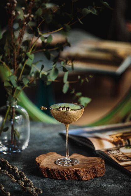 Seitenansicht des Alkoholcocktails mit Kiwi in einem goldenen Glas auf einem Holzständer