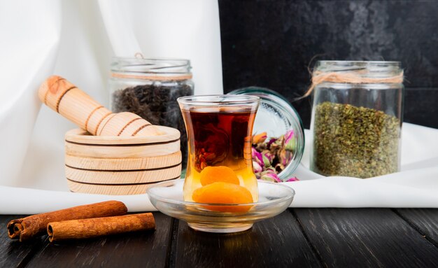 Seitenansicht des Armudu-Glases Tee mit getrockneten Aprikosen und Zimtstangen auf rustikalem