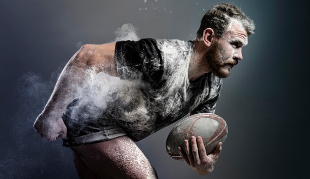 Seitenansicht des athletischen männlichen Rugbyspielers, der Ball mit Staub hält