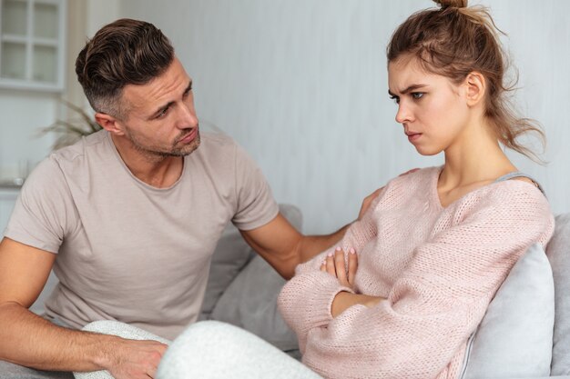 Seitenansicht des aufmerksamen Mannes sitzend auf Couch und seine beleidigte Freundin zu Hause beruhigend