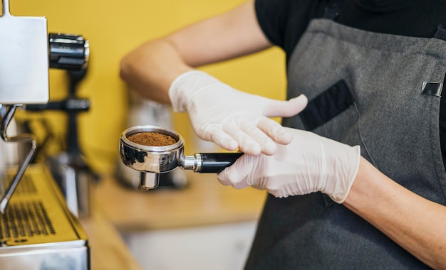 Seitenansicht des Barista mit Latexhandschuhen, die Kaffee für Maschine vorbereiten