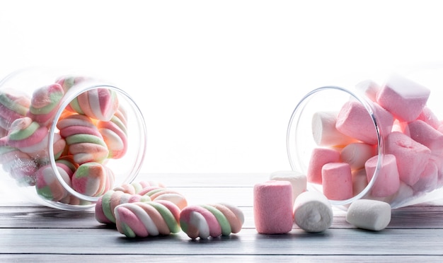 Seitenansicht des bunten verdrehten Marshmallows, der von einem Glas auf Weiß verstreut wird