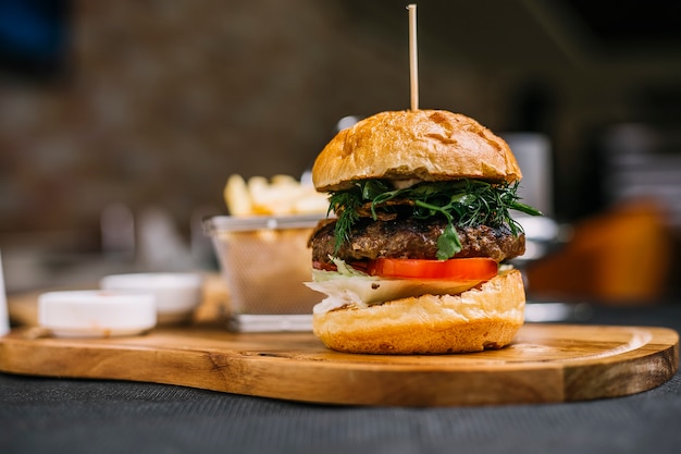 Seitenansicht des Burgers mit Rinderschnitzelkräutern und der Tomate auf einem Holzbrett