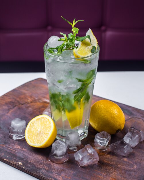 Seitenansicht des Cocktail Mojito mit Eis und Zitrone auf einem Holzbrett