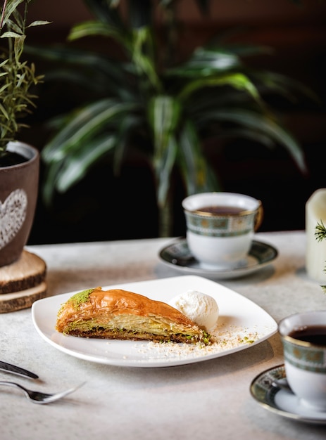 Seitenansicht des dreieckigen baklava der türkischen süßigkeiten mit pistazie, serviert mit eisbällchen auf teller