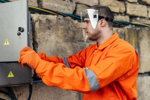 Seitenansicht des Elektrikers in Uniform mit Schutzhandschuhen und Gesichtsschutz