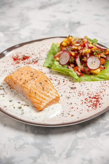 Seitenansicht des Fischmehls und des köstlichen Salats auf einem Teller auf befleckter weißer Oberfläche