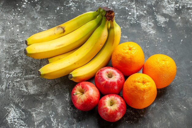 Seitenansicht des frischen Bananenbündels der organischen Nahrungsquelle und der roten Äpfel und der Orange auf dunklem Hintergrund