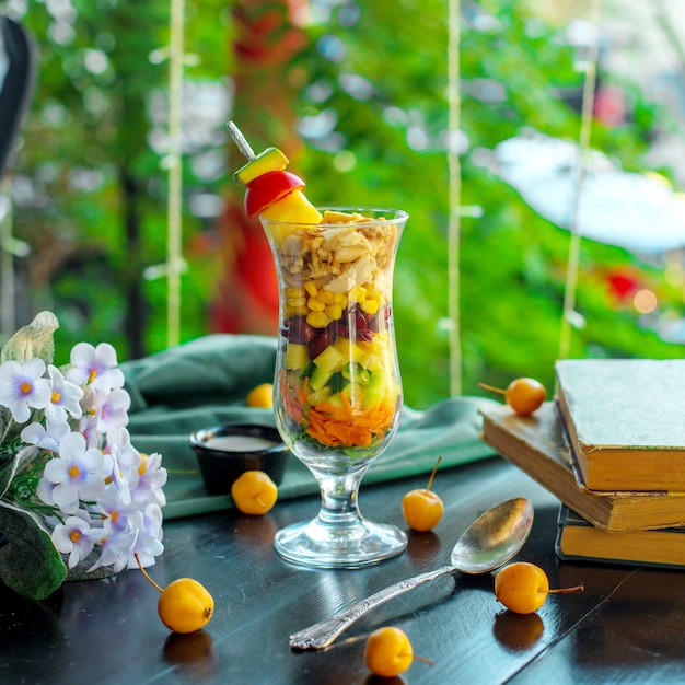 Seitenansicht des frischen Gemüsesalats Karottengurken-Ananas-Körner in einem Glas auf Holztisch