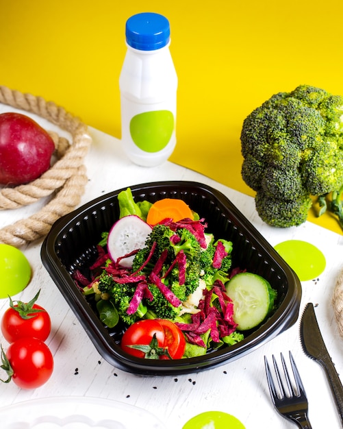 Seitenansicht des frischen Gemüsesalats mit Radieschen-Rotkohl-Karotte und Brokkoli in einer Lieferbox auf dem Tisch