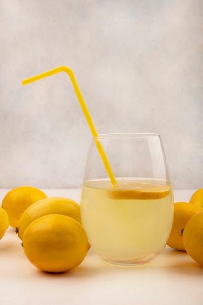 Seitenansicht des frischen Zitronensaftes in einem Glas mit Zitronen lokalisiert auf einer weißen Oberfläche