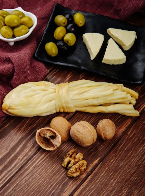 Seitenansicht des Frischkäses in Dreiecksform mit eingelegten Oliven auf einem schwarzen Tablett und Walnüssen mit Schnurkäse auf dunklem Holz