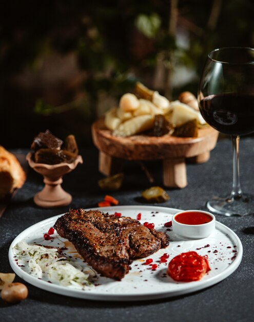 Seitenansicht des gegrillten Rindersteaks mit Ketchup und frischen Zwiebeln auf einem weißen Teller