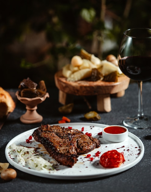 Seitenansicht des gegrillten Rindersteaks mit Ketchup und frischen Zwiebeln auf einem weißen Teller