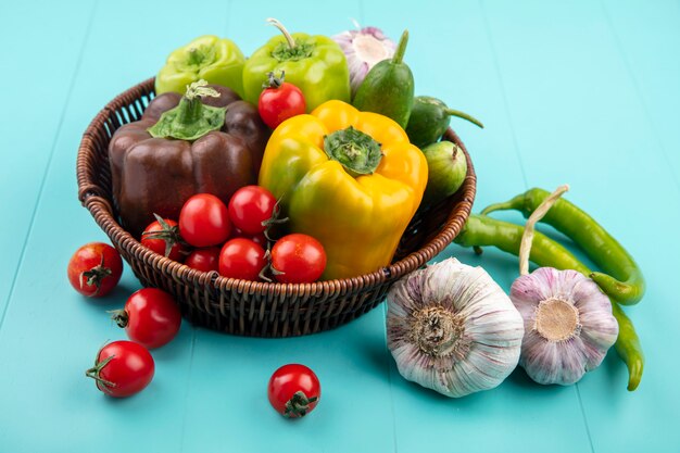 Seitenansicht des gemüses als pfeffer-tomaten-gurken-knoblauch im korb und auf blau