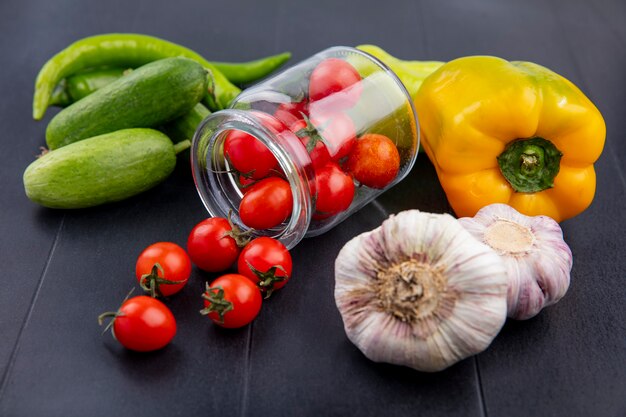 Seitenansicht des Gemüses als Tomaten, die aus Glas Knoblauchgurke und Pfeffer auf Schwarz verschüttet werden